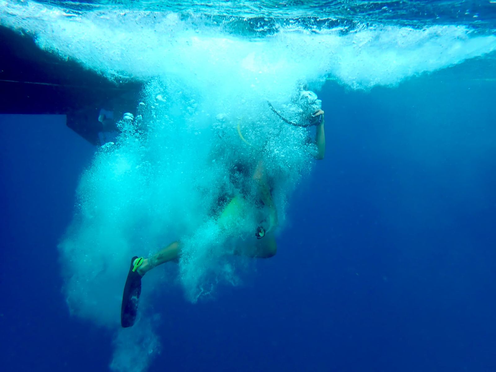 A diver descending through a cloud of bubbles under the boat